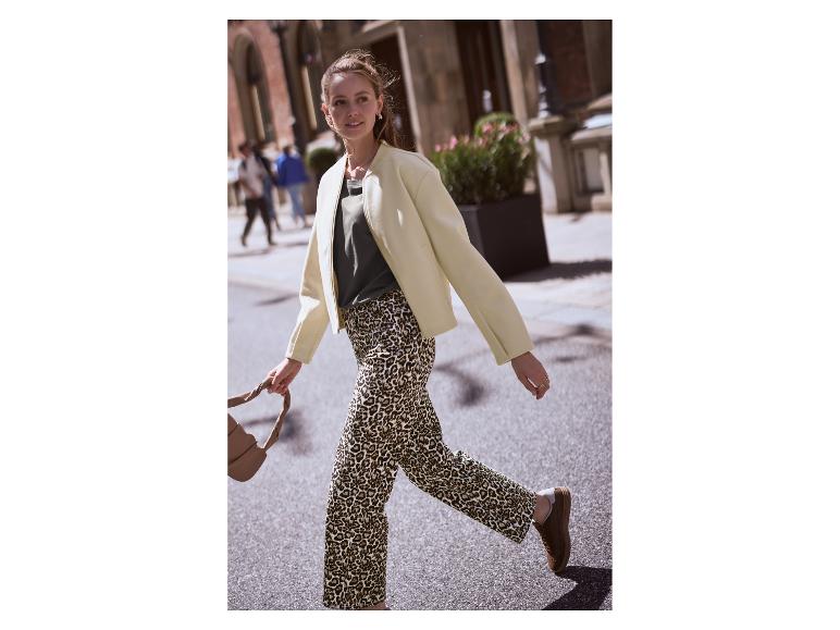 Frau in heller Jacke, grünem T-Shirt und Leopardenhose geht auf der Straße.