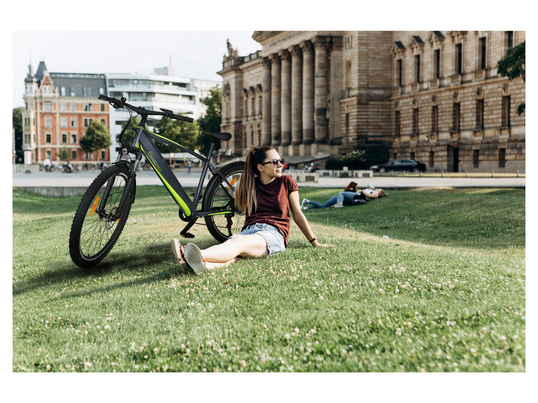 Eine Frau sitzt neben einem grünen Gazelle E-Bike in einem Park.