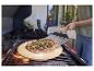 Pizza auf einem Pizzastein auf einem Grill, mit einer Person, die einen Pizzaschieber benutzt.