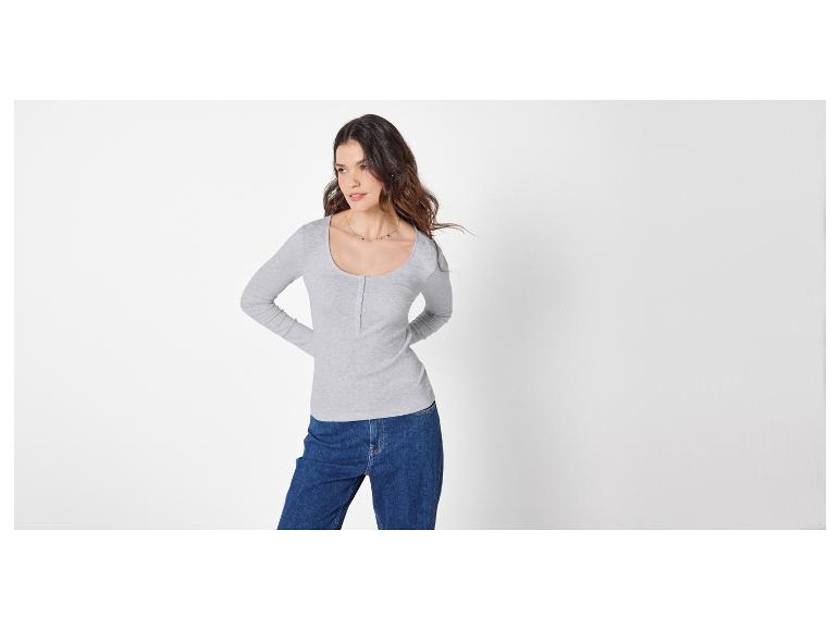 Frau in hellgrauem Langarmshirt und blauen Jeans, zur Seite blickend.