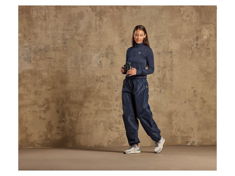 Eine Frau trägt eine blaue Regenhose und einen dunkelblauen Kapuzenpullover.