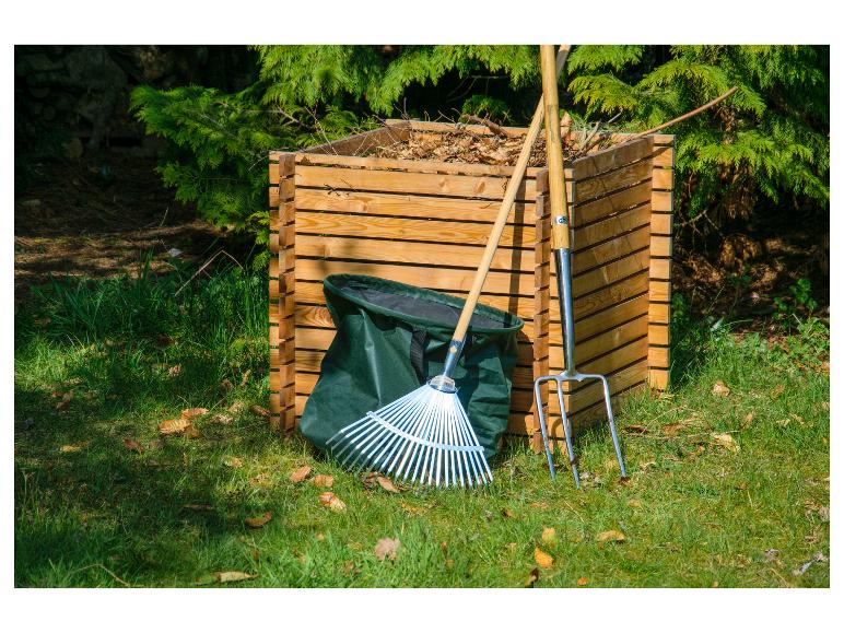 Komposter mit Rechen, Grabegabel und grünem Gartensack auf Gras.