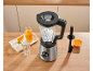 Mixer mit Eis, Orangensaft und einer Orange auf einer Holzküchenarbeitsplatte.