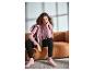 Frau in rosa Hoodie, geripptem Top, schwarzer Hose und rosa Sneakern auf einem Sofa.