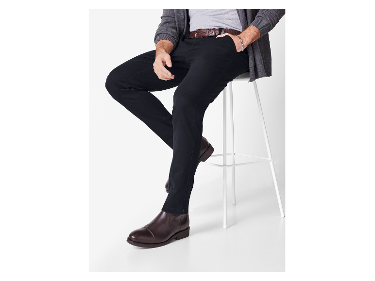 Ein Mann sitzt auf einem weißen Hocker in einer schwarzen Hose und braunen Schuhen.