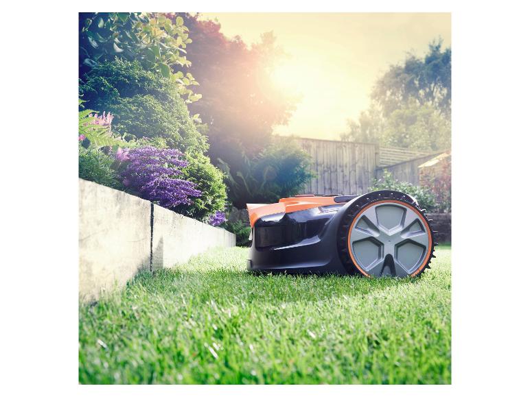 Orange-schwarzer Mähroboter auf grünem Rasen mit Blumen und strahlendem Sonnenschein.