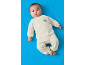 Baby in hellem Schlafanzug mit gesticktem Bären, liegend auf blauem Hintergrund.