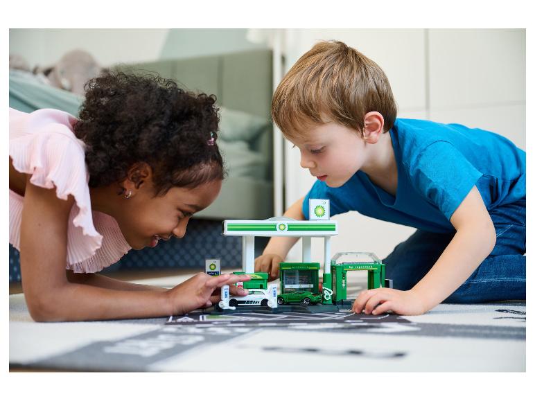 Zwei Kinder spielen auf dem Boden mit einem BP-Spielset, inklusive Tankstelle.
