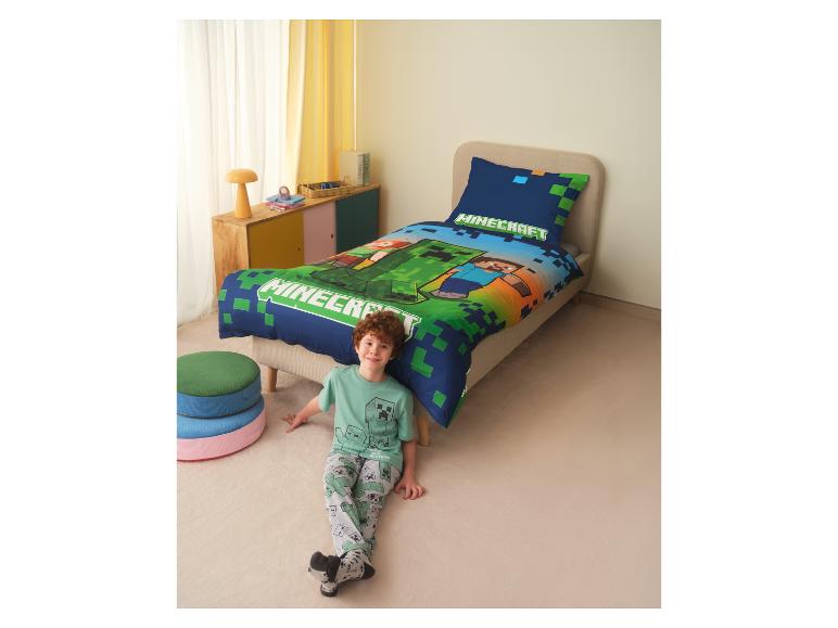 Junge im Gaming-Pyjama sitzt neben einem Bett mit passender Bettwäsche.