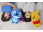 Zwei lächelnde Kinder liegen auf einem Teppich mit zwei Plüschtieren, einem blauen und einem gelben.