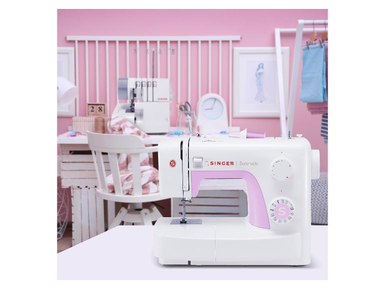 Weiße Nähmaschine mit rosa Akzenten auf einem Tisch in einem rosa Nähzimmer.