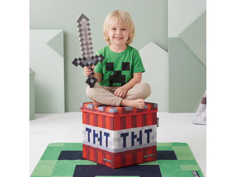 Lächelndes Kind mit Spielzeugschwert, sitzt auf einer TNT-Block-Aufbewahrungsbox, auf einem Videospiel-Teppich.