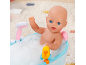 Puppe in Badewanne mit Schaum, spielt mit einer gelben Ente.