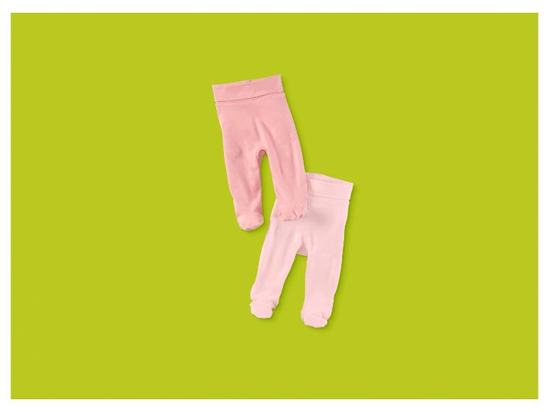 Zwei Paar rosa Babyhosen mit Füßen auf grünem Hintergrund.