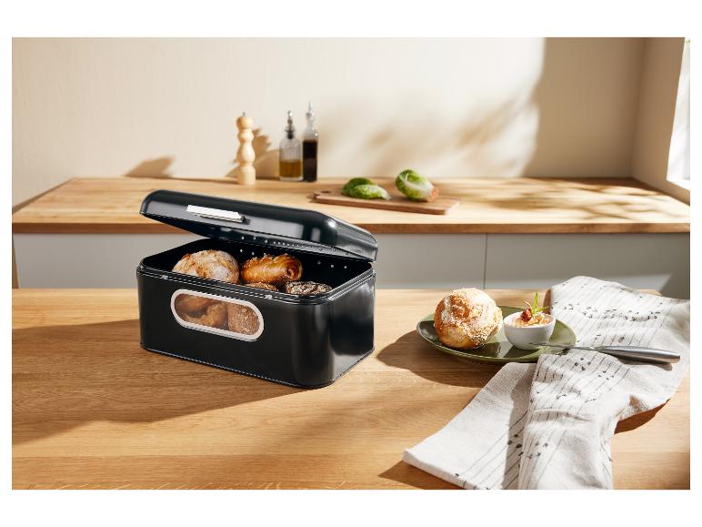 Schwarzer Brotkasten gefüllt mit Brötchen und Gebäck auf einer Holztheke.