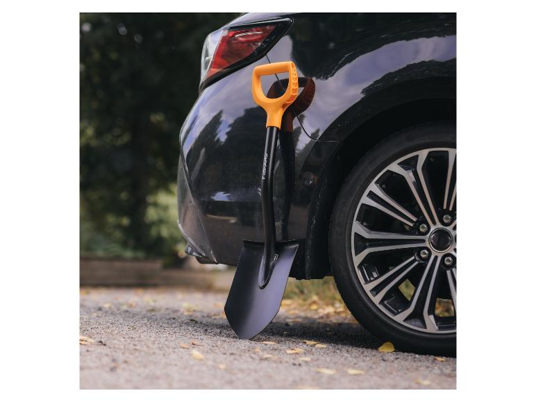 Schwarzes Auto und Spaten mit orangefarbenem Griff auf Schotterweg.