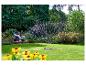 Frau und Mädchen auf Bank im Garten, Rasen wird mit Sprinkler bewässert.