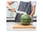 Person in Schürze schneidet Wassermelone mit einem Nicer Dicer Messer auf einem Schneidebrett.