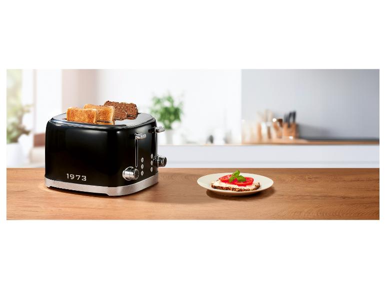 Schwarzer Toaster mit Toast und ein Teller mit Tomatenbrot auf einem Holztisch.