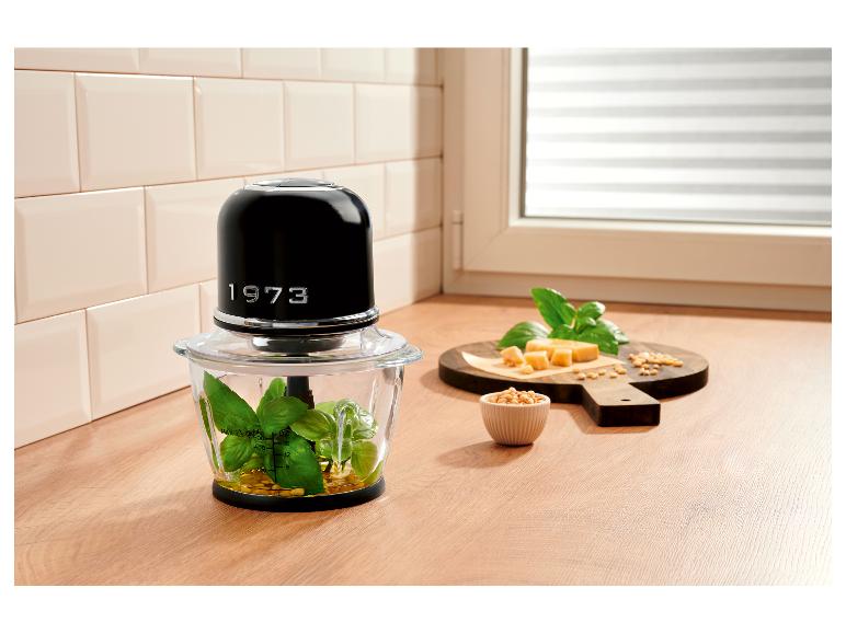 Schwarzer Zerkleinerer mit Pesto-Zutaten auf Holzbrett in der Küche.