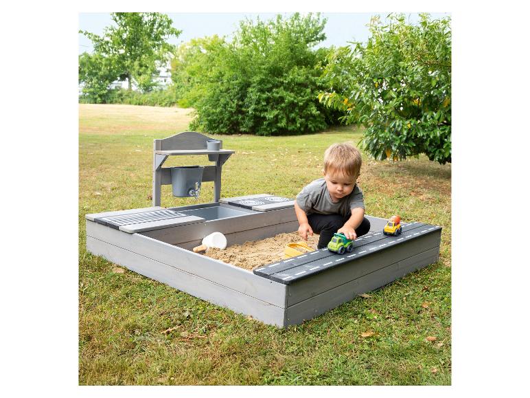Junge spielt im Sandkasten mit Wassertisch und Spielzeugautos im Garten.