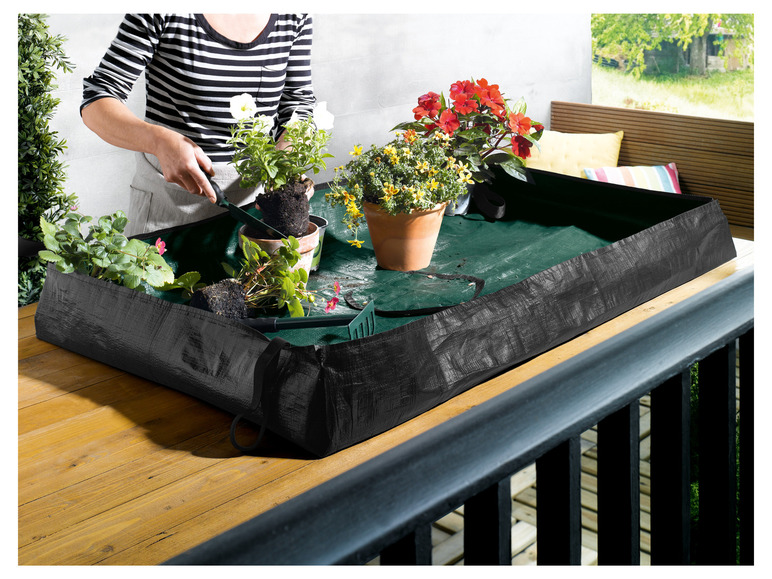 Ein schwarzer Pflanzenbehälter auf einem Holzbalkon, gefüllt mit verschiedenen Pflanzen.