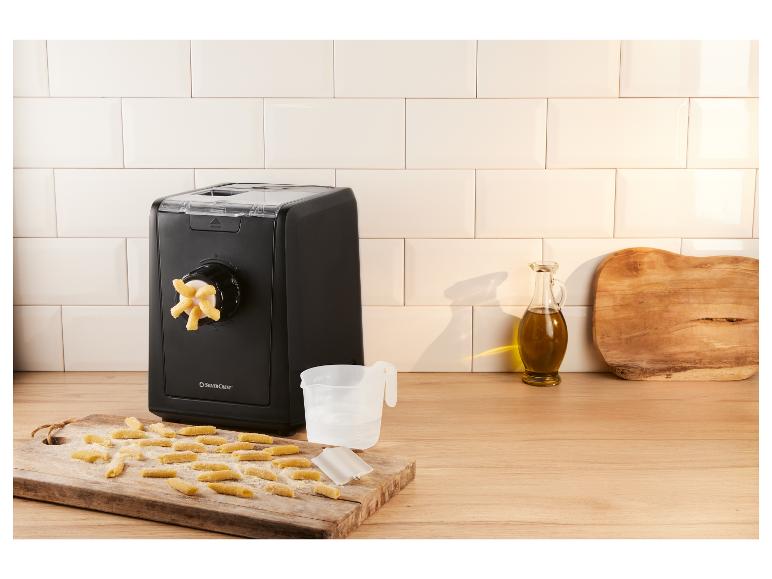 Schwarze Nudelmaschine mit frischen Nudeln auf einem Holzbrett.
