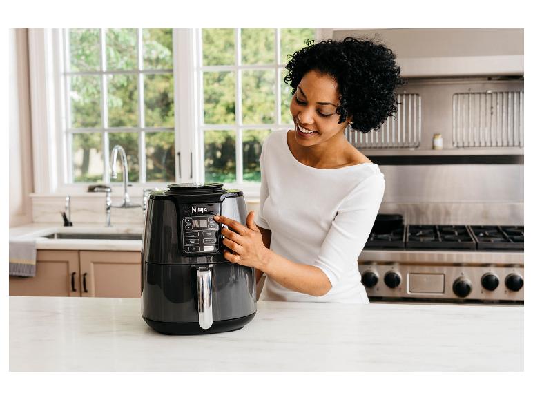 Frau in der Küche benutzt eine Heißluftfritteuse, lächelt und schaut auf das Gerät.