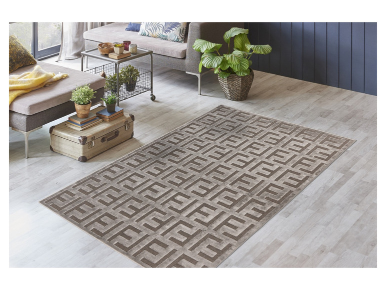 Ein grauer Teppich mit geometrischem Muster in einem hellen Wohnzimmer.