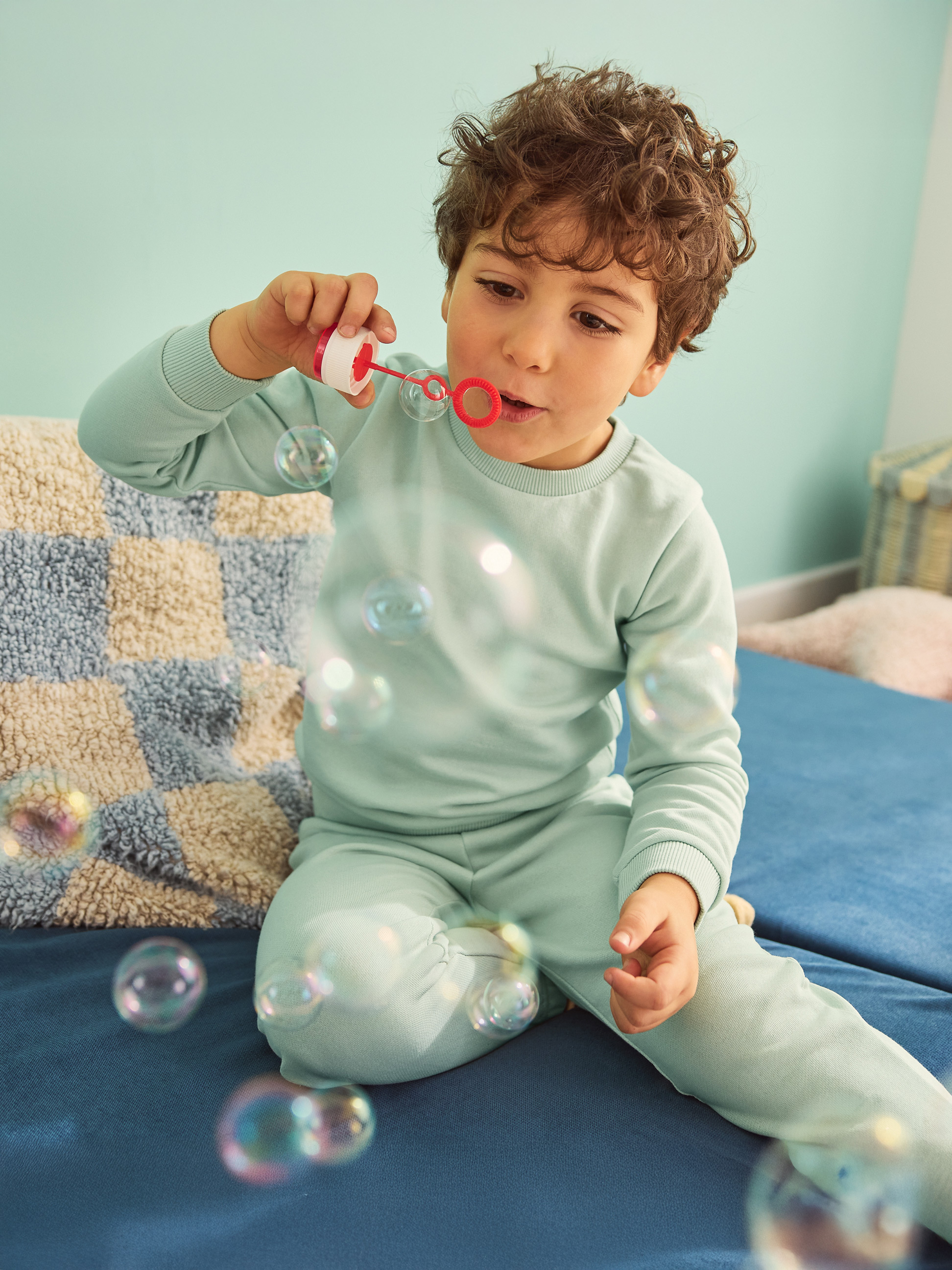 Junge im blauen Pyjama bläst Seifenblasen auf einem blauen Sofa.