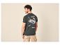 Mann von hinten in dunkelgrünem T-Shirt mit Bergaufdruck und beiger Shorts.