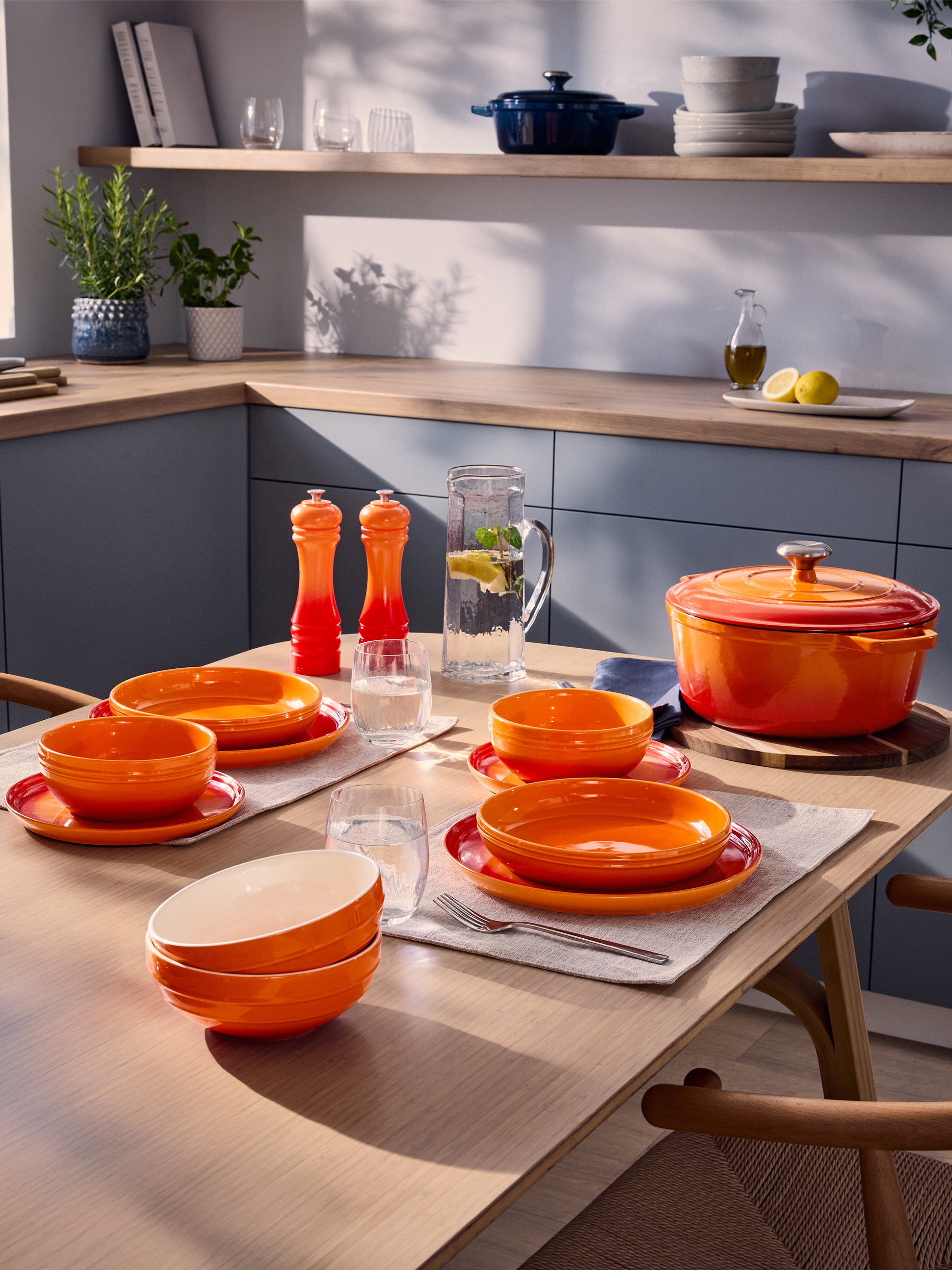 Oranges Geschirr und Gusseisentopf auf einem Küchentisch mit Kräutern und Kochutensilien.