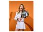 Frau in weißer Sportkleidung mit Padel-Schläger vor orangefarbenem Hintergrund.