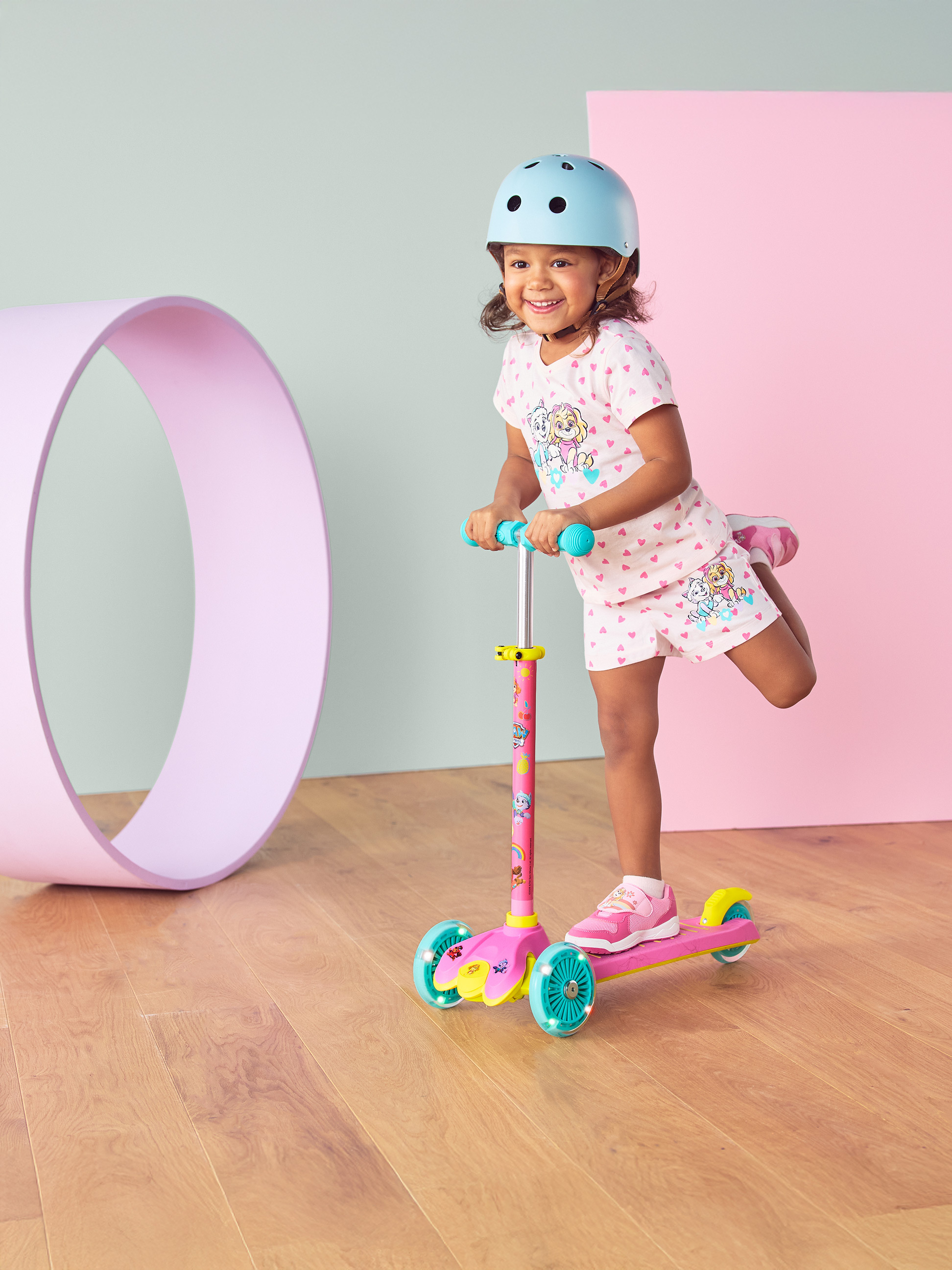 Mädchen mit Helm und rosa Roller mit leuchtenden Rädern, lächelnd.