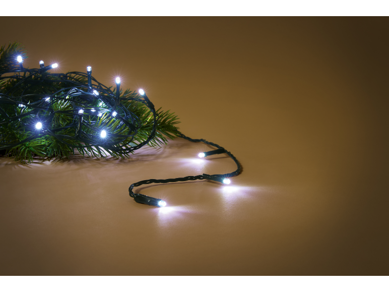 Weiße LED-Weihnachtsbeleuchtung auf einem grünen Tannenzweig, auf warmbraunem Hintergrund.