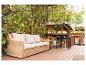Geflochtenes Outdoor-Sofa mit beigen Kissen und Grill auf einer Holzterrasse.
