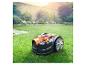 Orange-schwarzer Mähroboter auf grünem Rasen in einem sonnigen Garten.