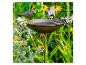 Vogeltränke mit Metallvogelfigur und lebender Kohlmeise, umgeben von blühenden Blumen.