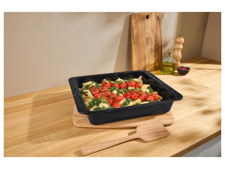 Schwarze Auflaufform mit Nudeln, Spinat und Kirschtomaten auf einer Holzarbeitsplatte.