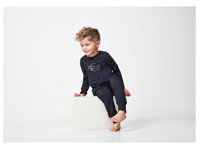 Ein Kleinkind in dunkelblauen Pyjamas sitzt auf einem weißen Hocker.