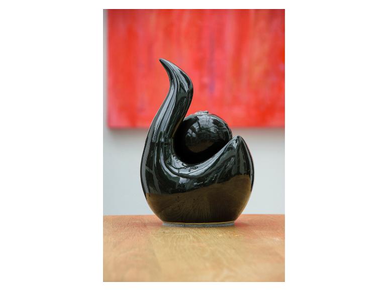 Eine glänzende schwarze Keramikskulptur mit wirbelndem Design und einer Kugel auf einer Holzoberfläche.