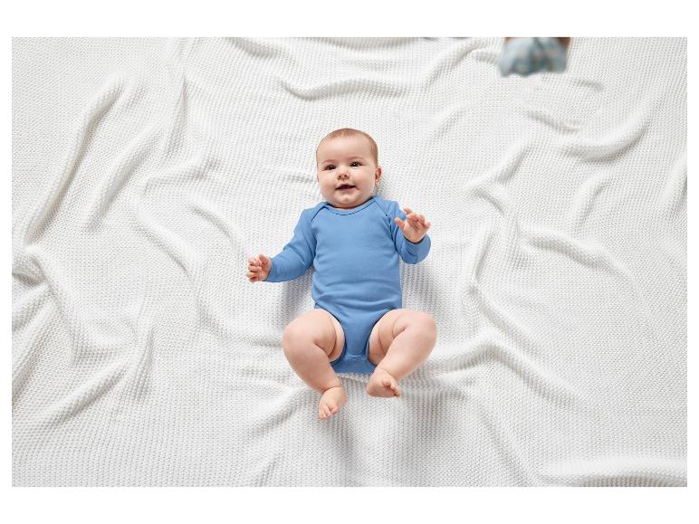 Ein Baby in einem blauen Strampler liegt auf einer weißen Decke.