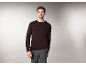 Ein Mann in einem dunkelbraunen Rundhals-Pullover und einer grauen Hose.