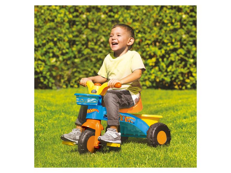 Ein Kind fährt im Garten auf einem Hot Wheels Dreirad.