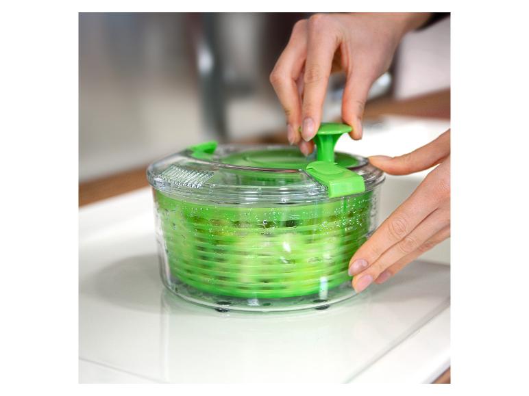 Hände benutzen eine grüne Salatschleuder, um Salat zu trocknen.