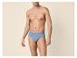 Mann in blauen Baumwollslips, posiert vor beigem Hintergrund.