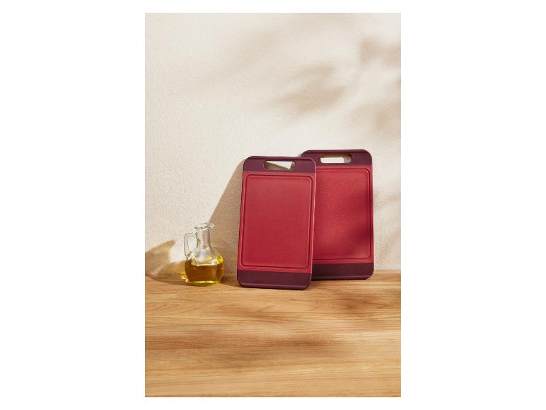 Zwei rote Schneidebretter und eine Ölkanne auf einem Holztisch.