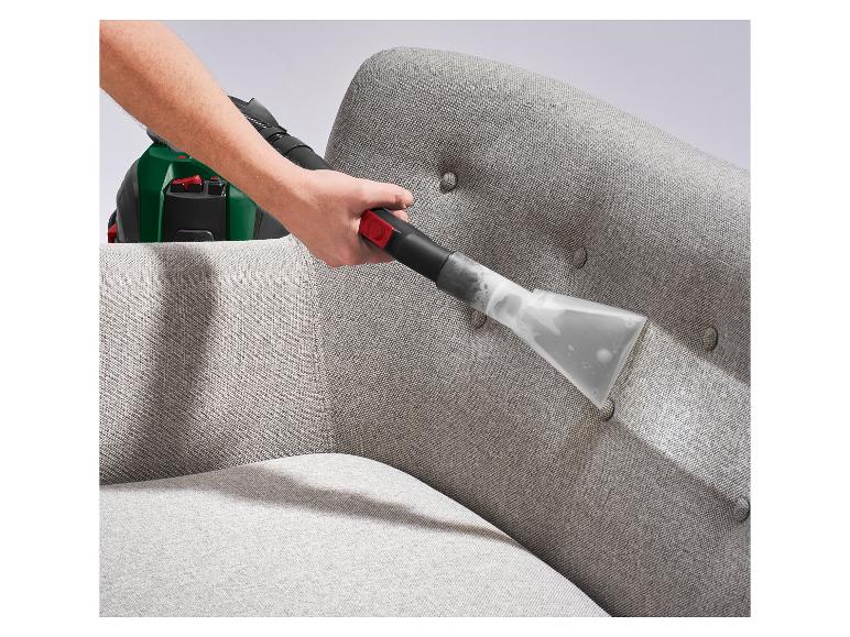 Hand reinigt ein graues Stoffsofa mit einem Polsterreinigungswerkzeug.