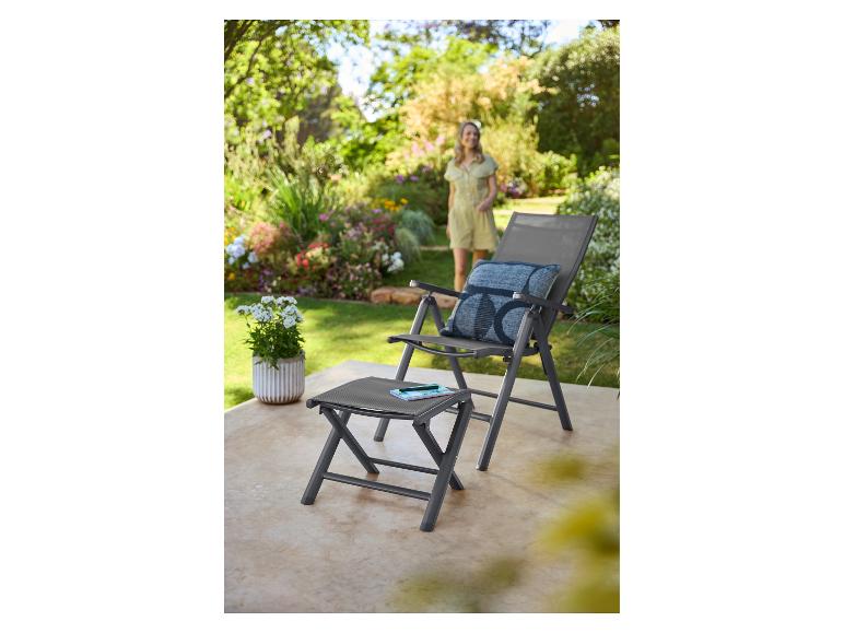 Grauer Gartenstuhl und Fußhocker auf einer Terrasse mit einer Frau im Hintergrund.