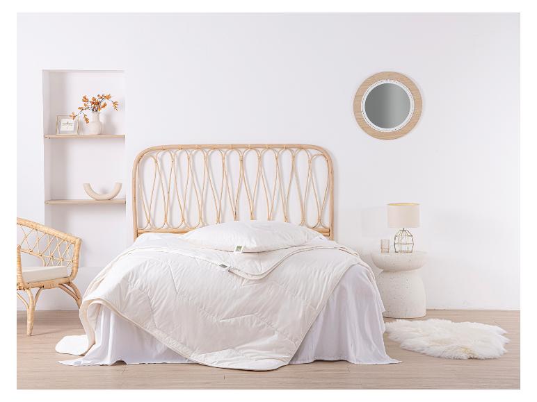 Schlafzimmer mit Rattanbett, weißer Bettdecke und Kissen, mit rundem Spiegel und Schaffellteppich.